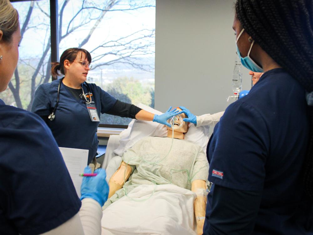 professional and student nurses gather around a patient simulator in the campus' patient simulator lab.