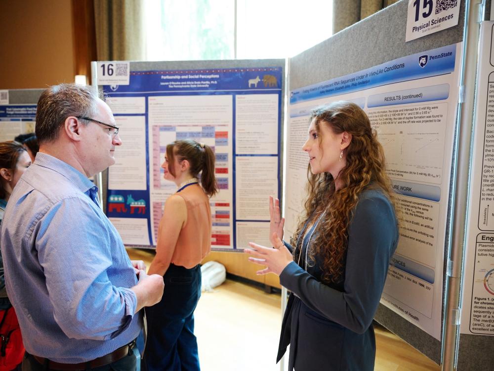 Faculty judge hearing explanation from student presenter in front of a research poster