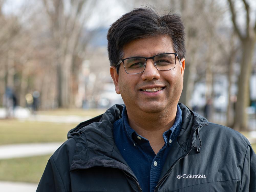 A person wearing glasses and a windbreaker poses for a photo outside