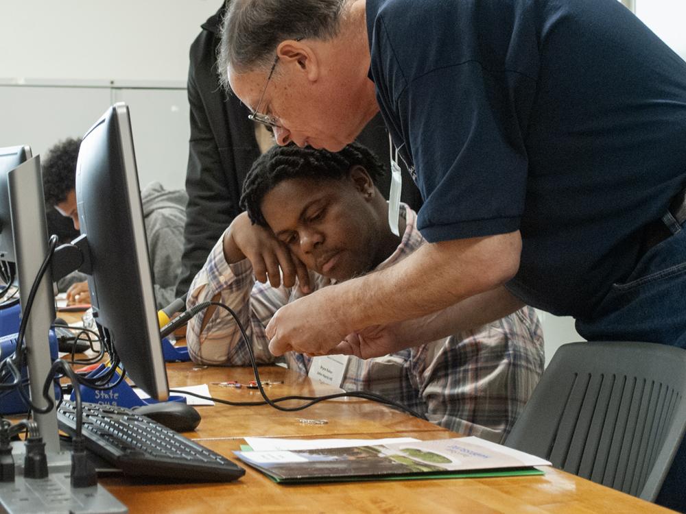 A Penn State Harrisburg faculty member helps a high school student with an activity, in front of computer monitors