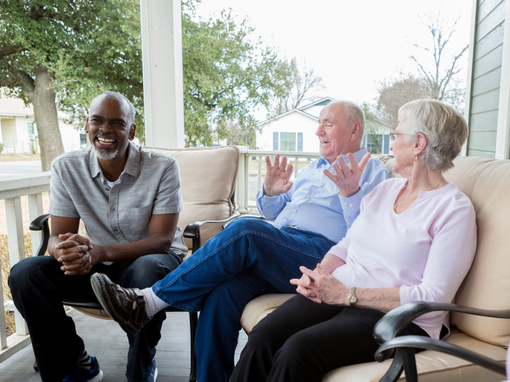 Three older adults sitting outside talking on a porch. 