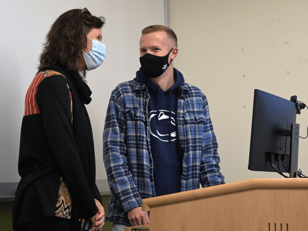 Harrison Brennan (right) stands at a podium with faculty adviser Bettina Brandt (left) during a Students Teaching Students lecture. 