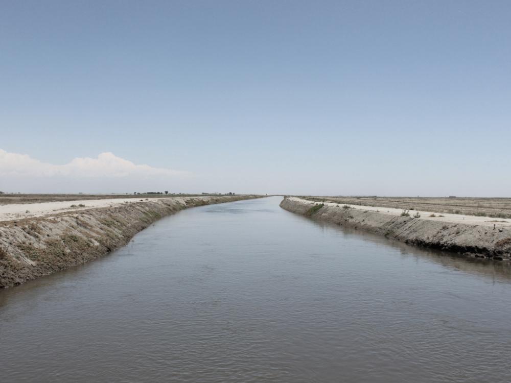A landscape image of a water channel with barren land on either side.