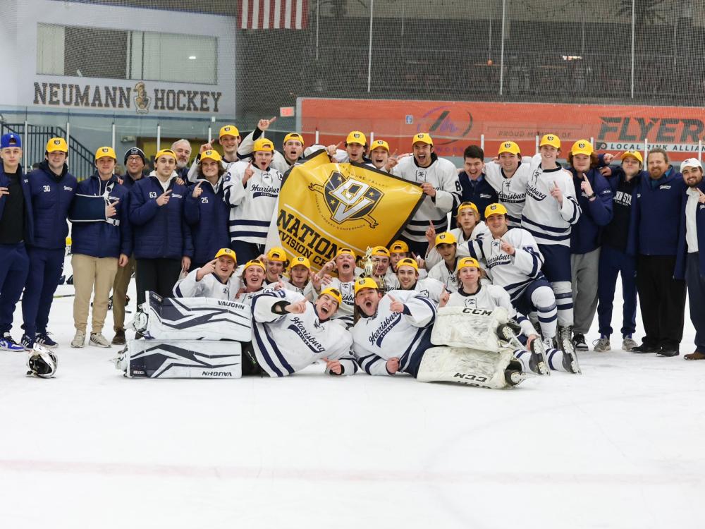 Penn State Harrisburg's ice hockey team on the ice, with players holding a championship banner