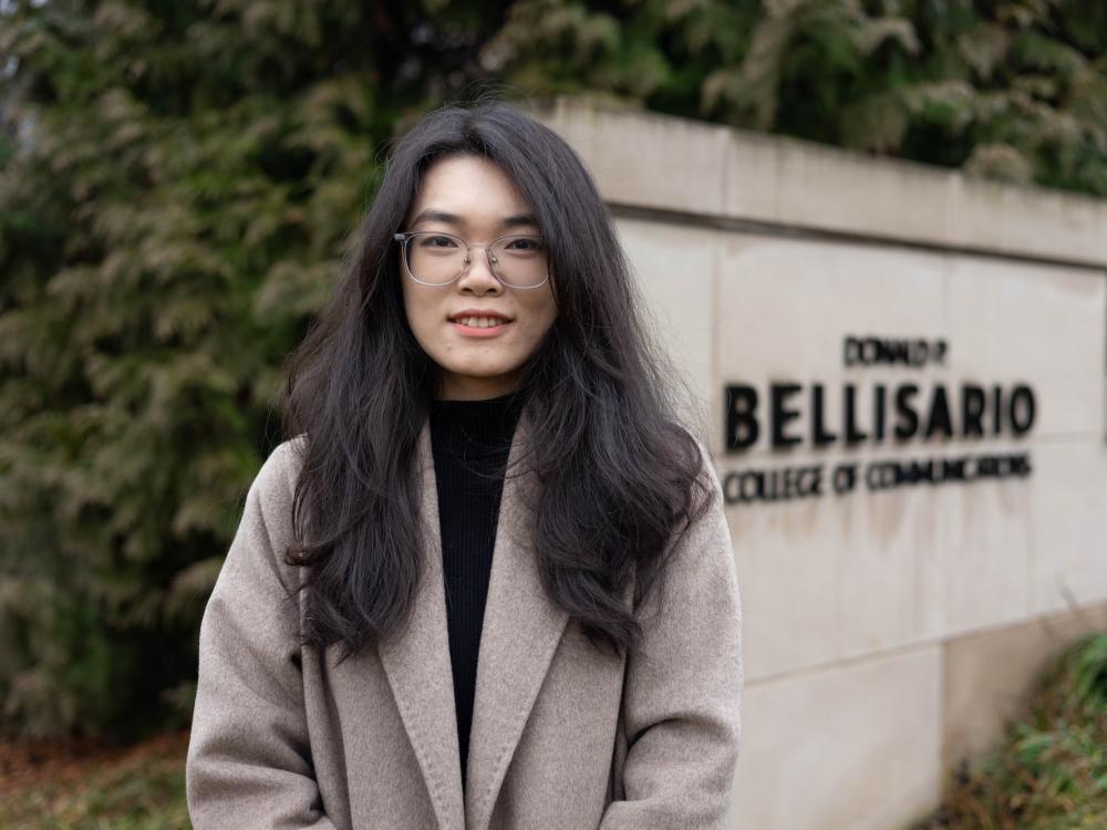 Maggie Liao standing outside Carnegie Building next to the sign for the Donald P. Bellisario College of Communications.