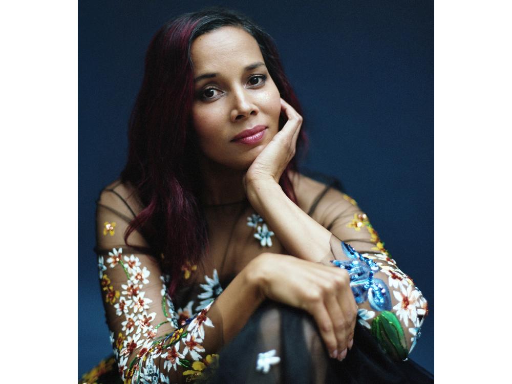 A woman of color sits with her knee pulled up to her chest and rests her chin in her hand.