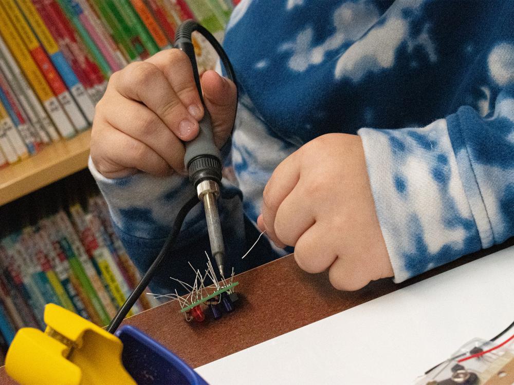 A middle school student holds a soldering iron during a Teen STEM program