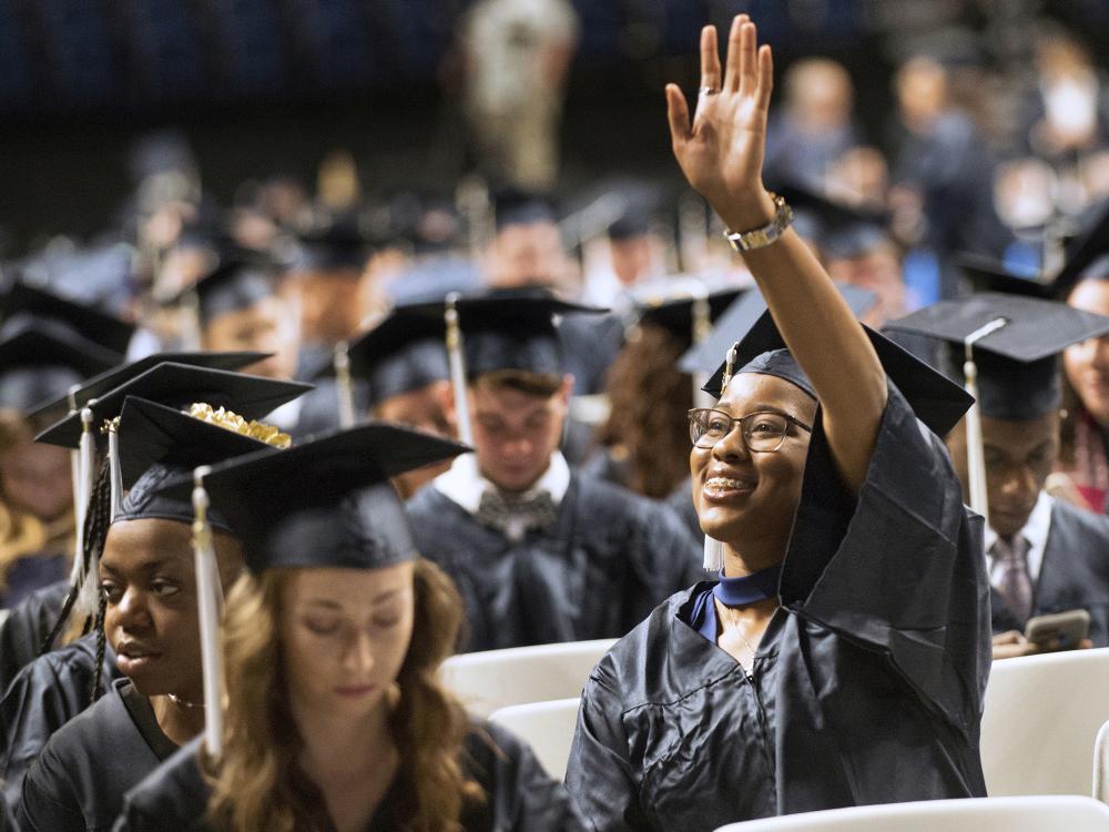 A graduate waves at Penn State commencement.