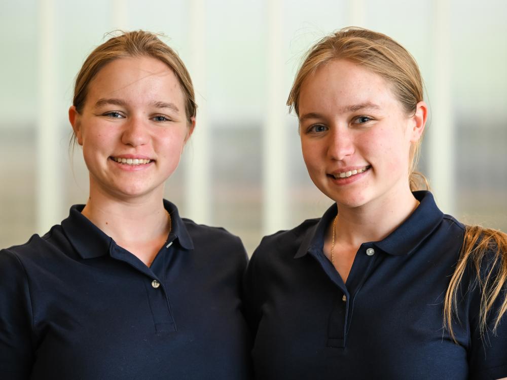 An indoors portrait of two individuals wearing blue polo shirts.