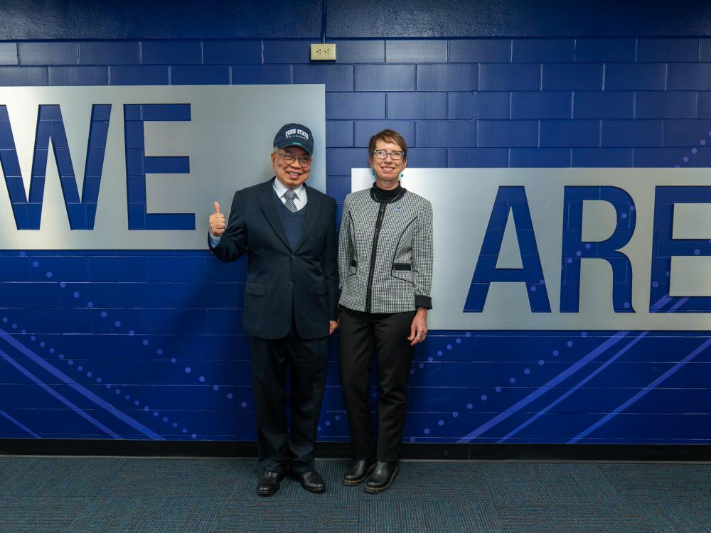 A man and a woman posing in front of a wall that says "We Are"
