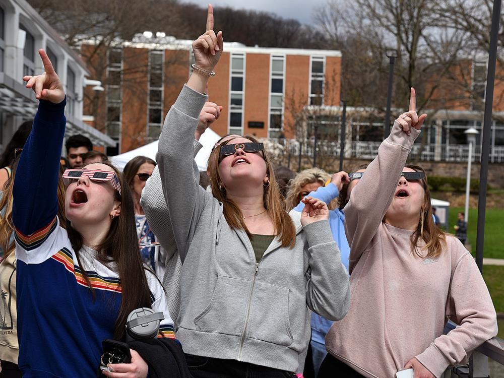 People wearing eclipse glasses pointing to sky