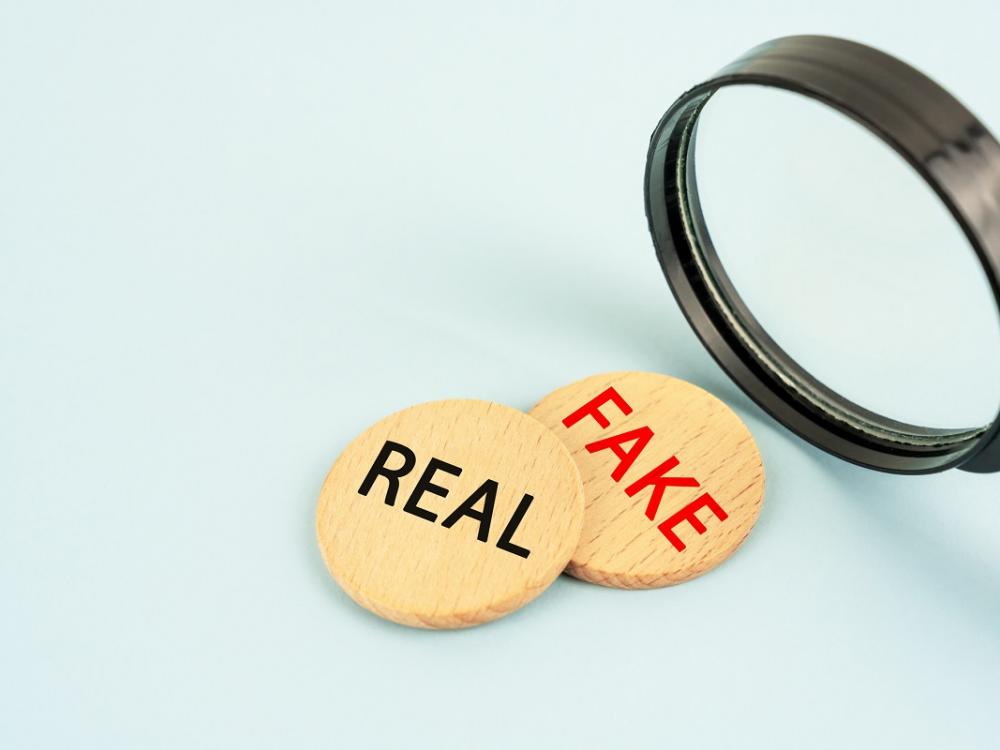A magnifying glass looks at two chips that say real and fake.
