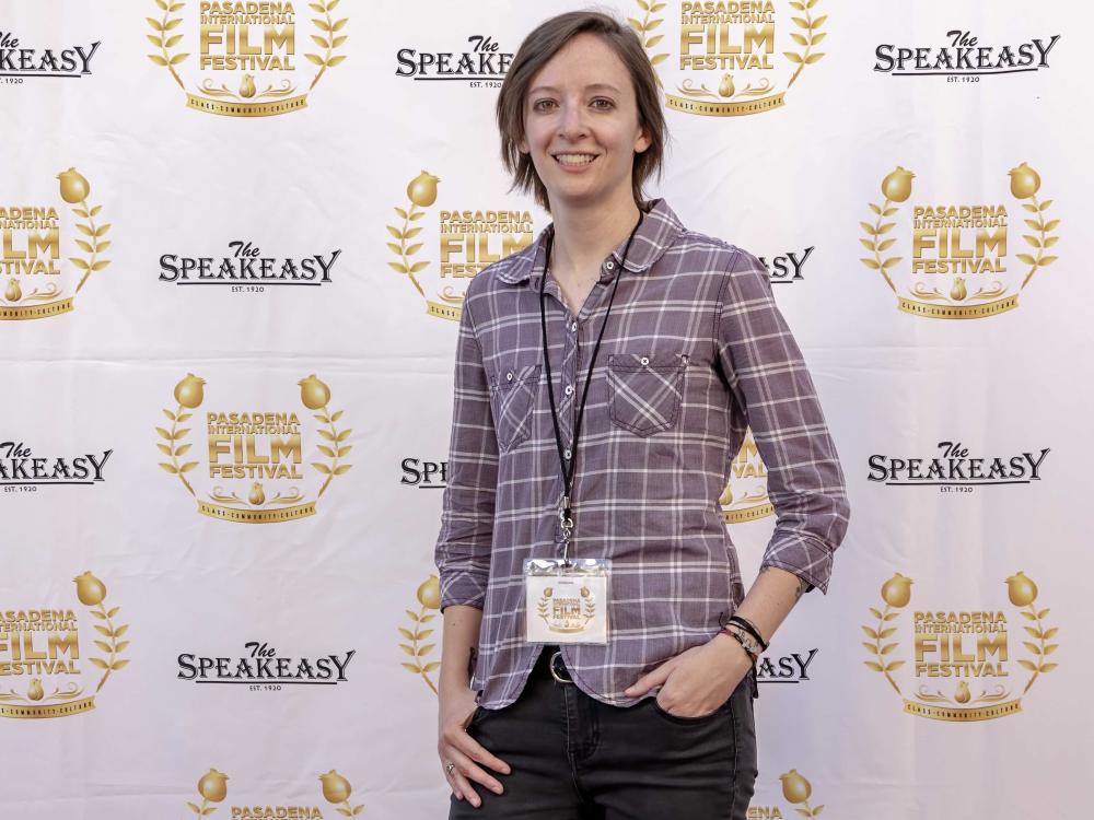 Brown haired woman stands with hands in pockets in front of a white screen