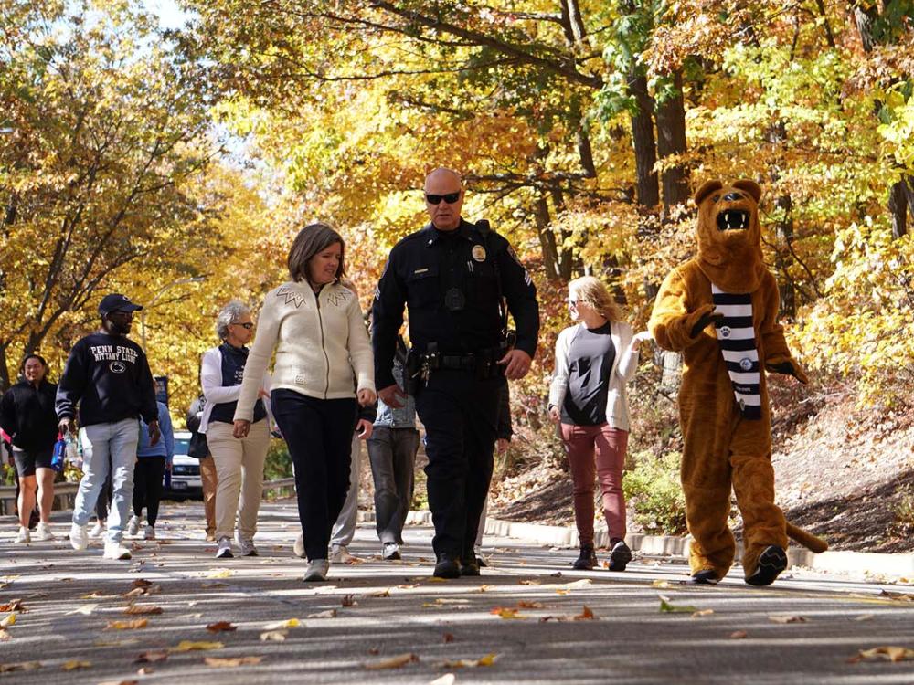 Group of people walking downhill on a road surrounded by fall foliage.