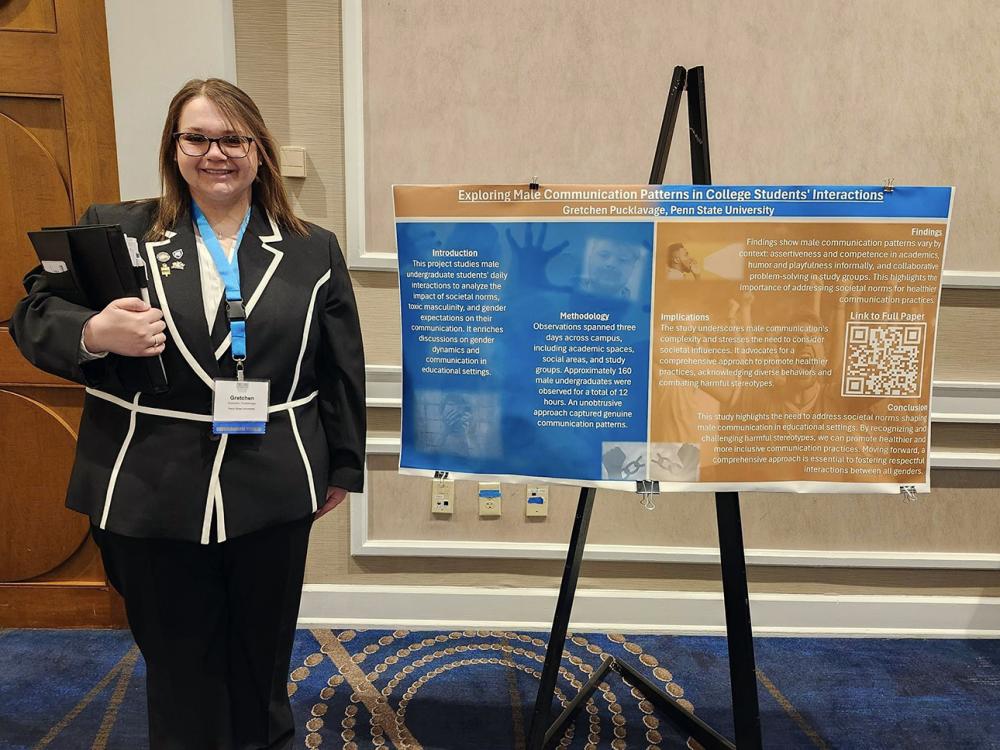 Female student holding folders and standing next to poster board positioned on an easel.