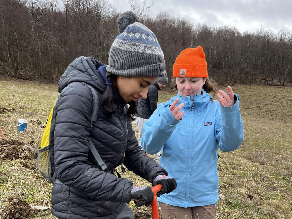 Two students dig with a shovel in a field outside