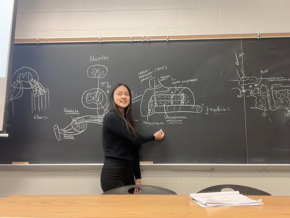 Lisa Wang illustrating a biology concept at a chalkboard