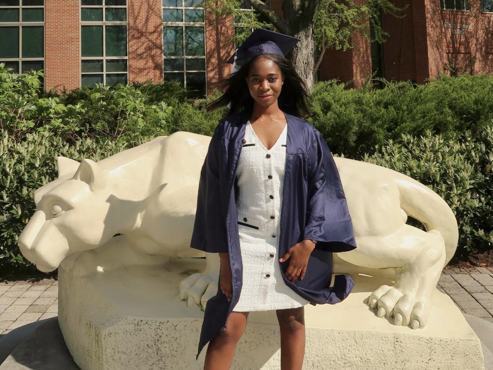 Mary Odei wears her cap and gown in front of the Nittany Lion statue at Penn State Harrisburg