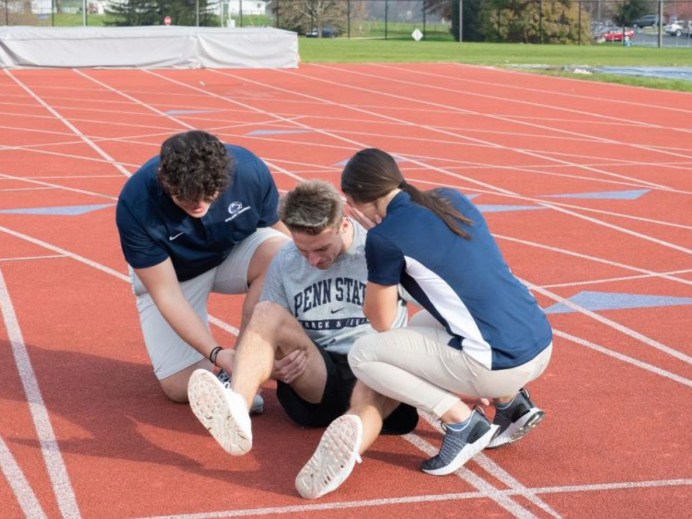 Two athletic training students work with a student athlete who has hurt themselves and needs medical attention.