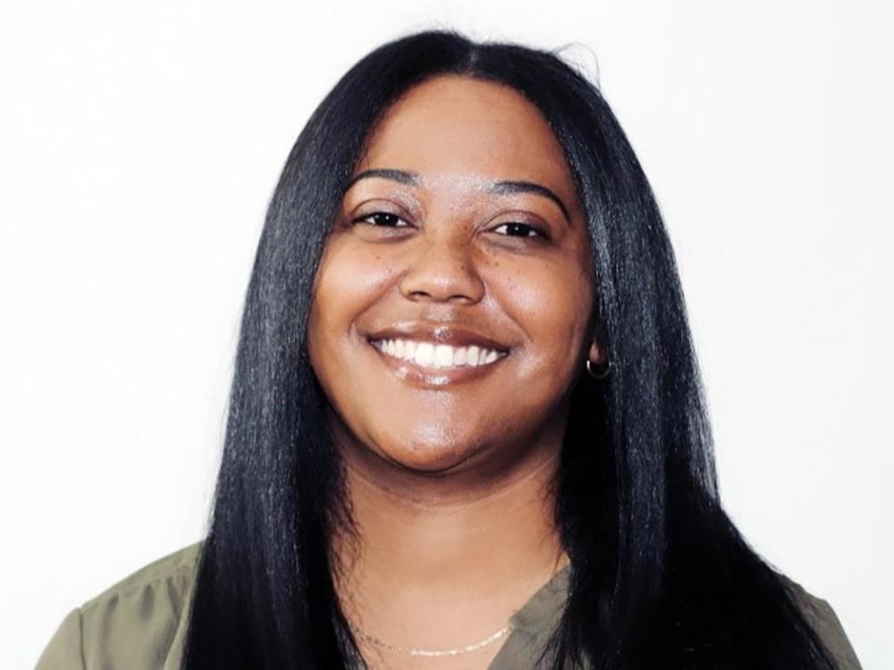 A photo of Maura smiling and wearing a green shirt on a white background