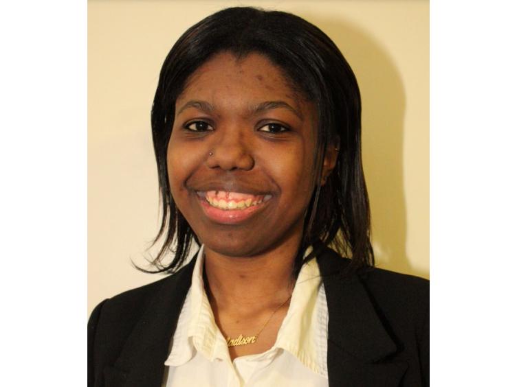 Head shot of a young Black woman wearing a black business suit and white shirt.