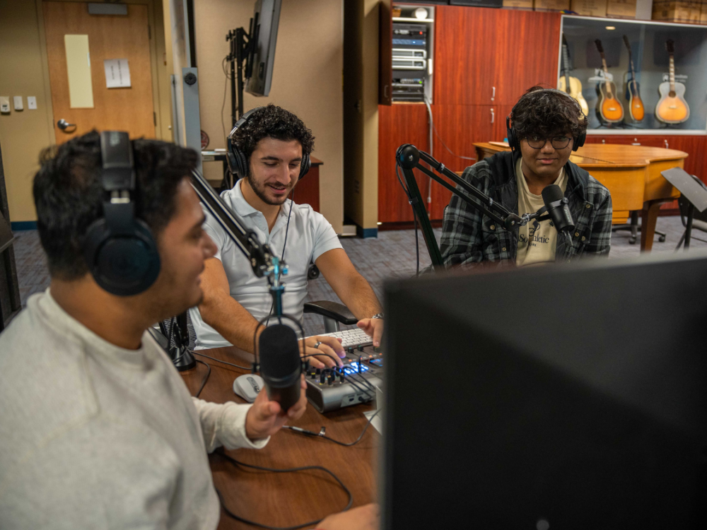 3 male students sitting in a podcasting booth 