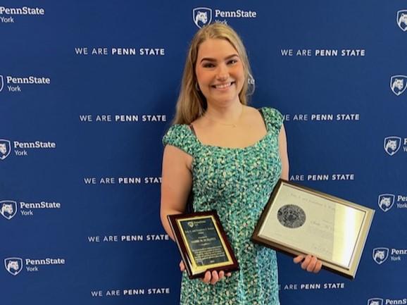 Person smiling, holding plaques, standing in front of blue backdrop.