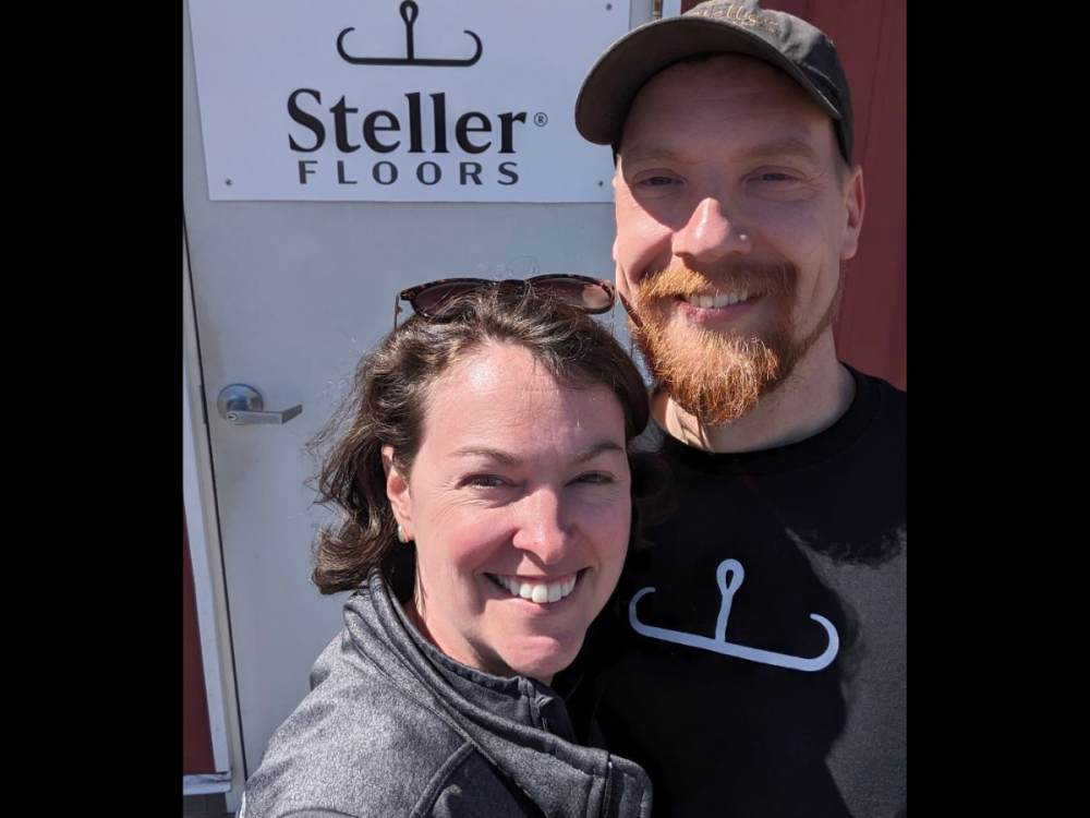 Britta and Evan stand in front of a sign that says Steller Floors