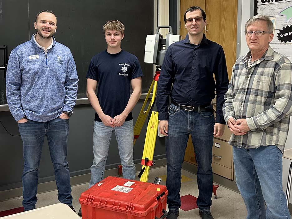 Four people standing next to each other with a blackboard behind them.