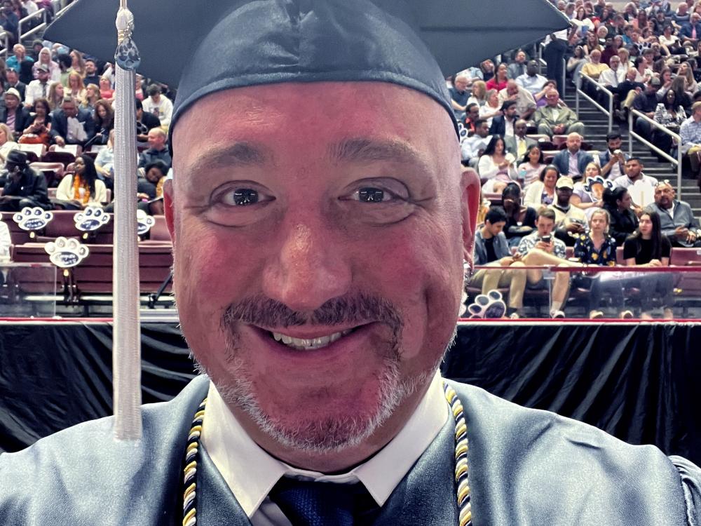 a man wearing a graduation cap and gown in front of stands in an arena