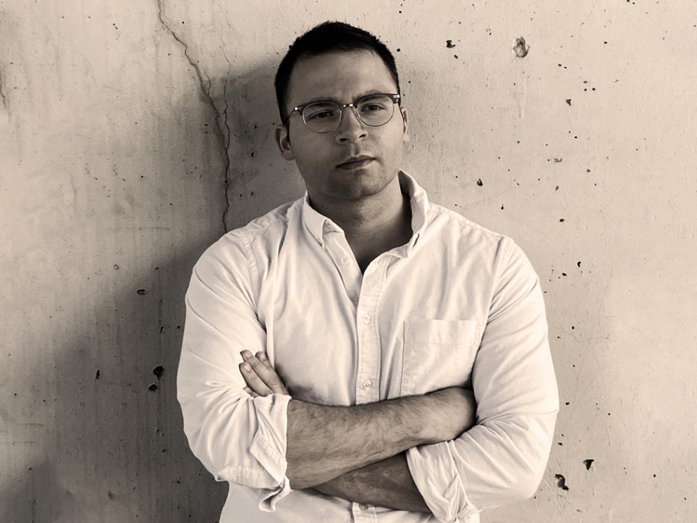 A black and white photograph of Dillon Brown leaning against a wall. 