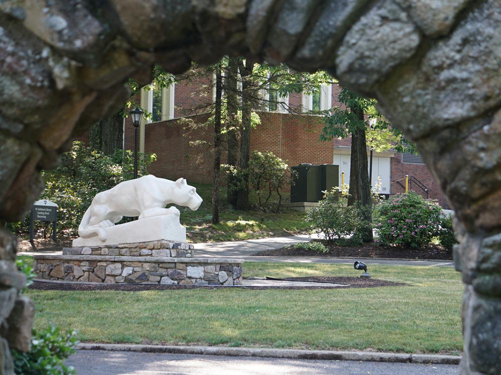 A stone lion statue in a grassy area with a stone archway in the foreground