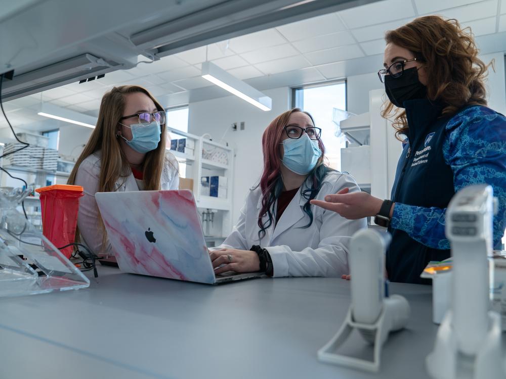 Three people around a laptop on a lab bench.