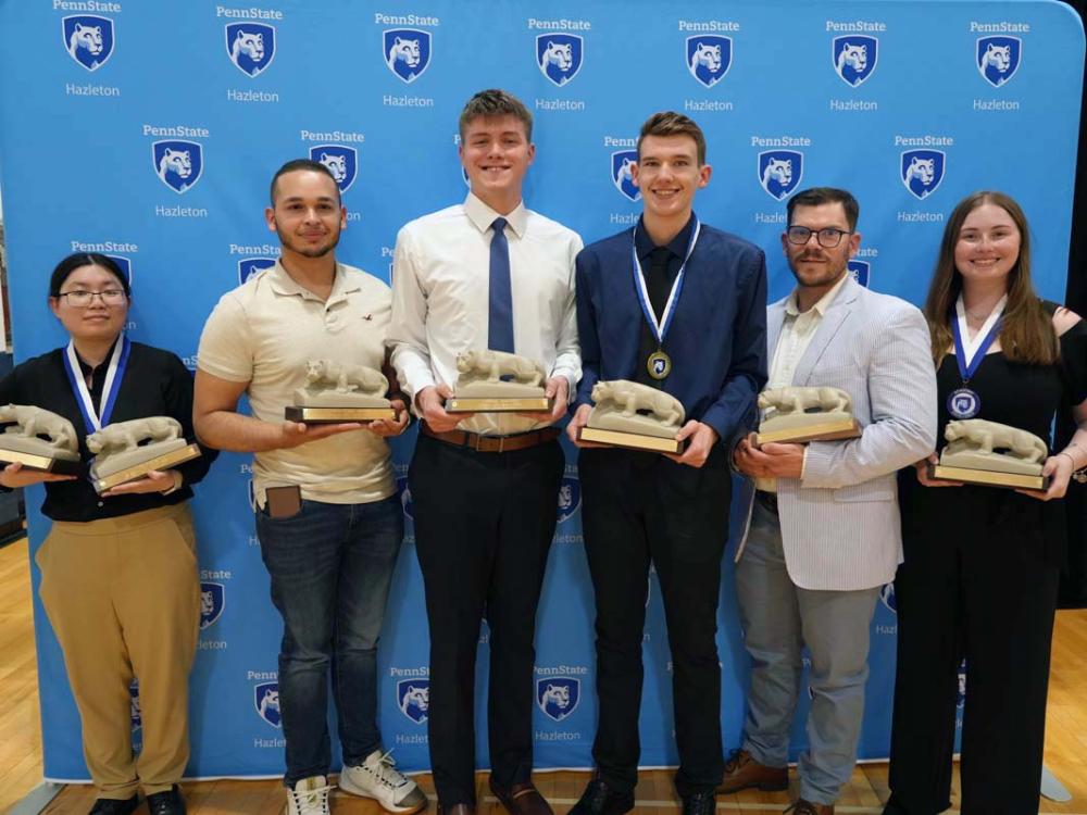 Group of six students standing in a row holding miniature lion statues