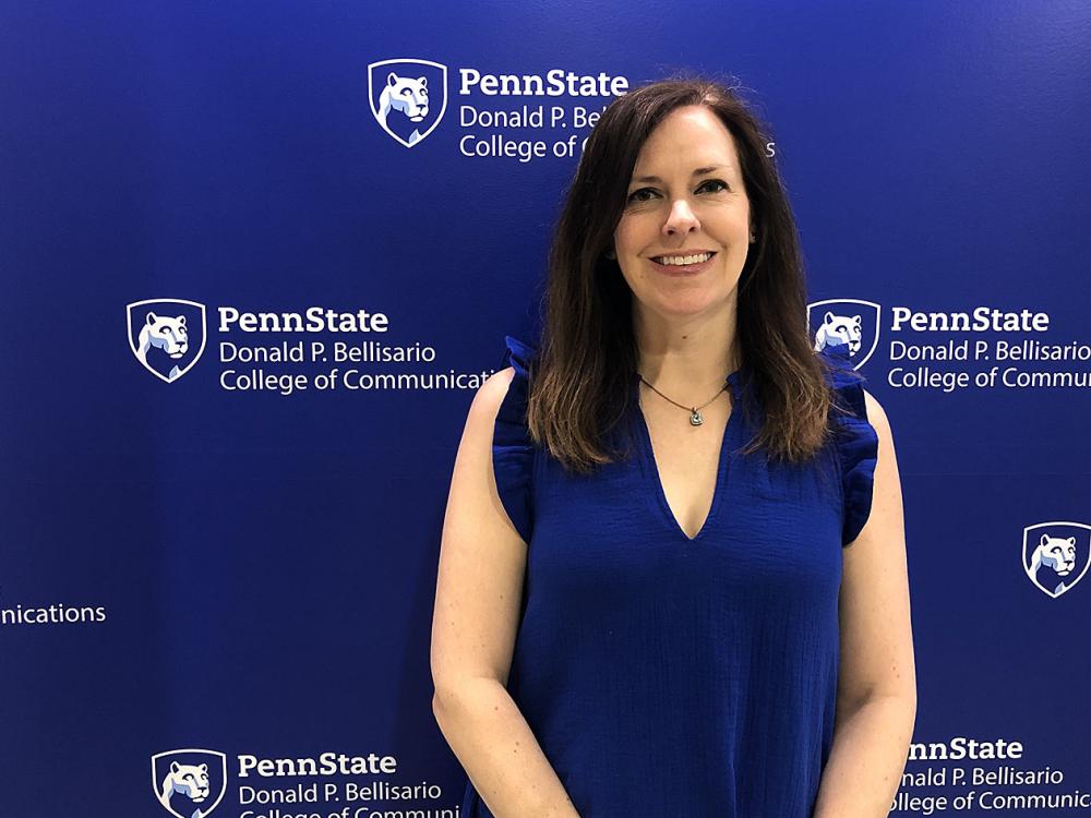 A dark-haired woman in a blue shirt stands in front of a blue-and-white wall