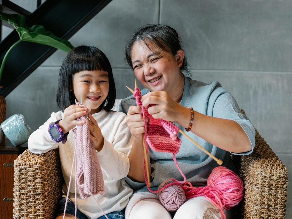 A child and an adult laughing and knitting