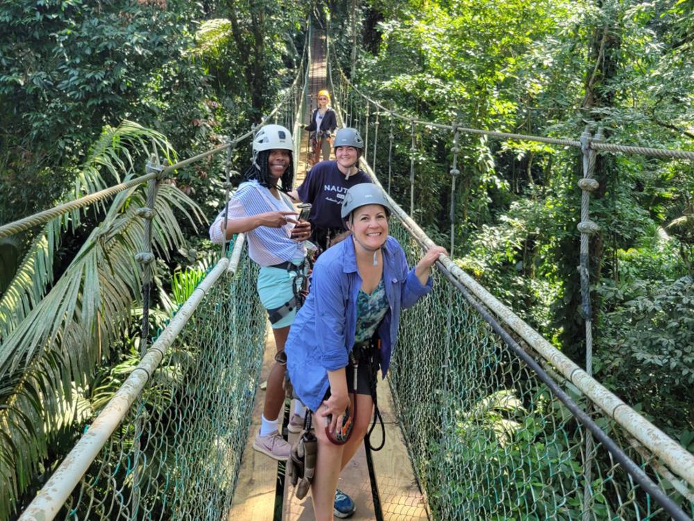 three women pose for a photo on a suspension bridge in the rain forest canopy