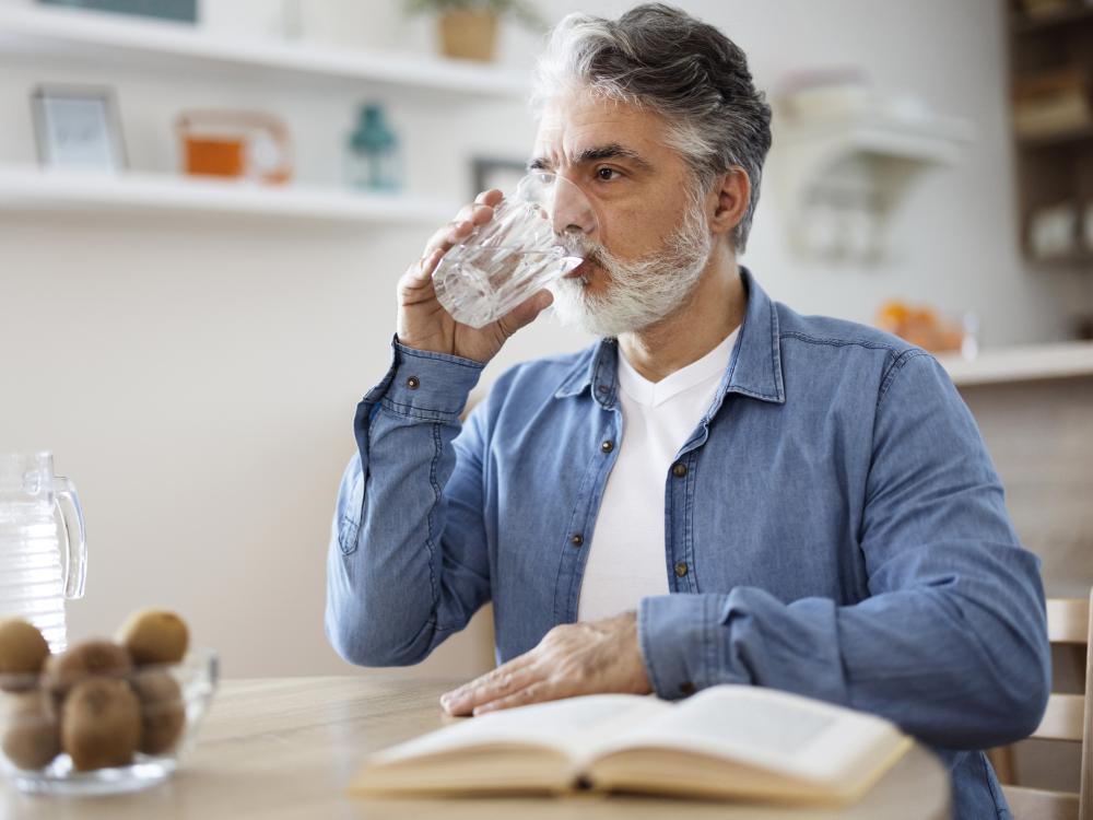 Older person sitting in a kitchen drinking water
