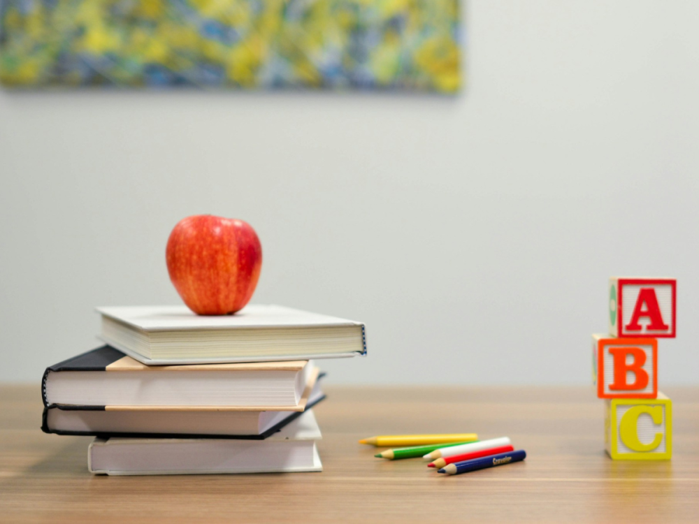 An apple resting on a stack of books on a desk next to ABC blocks
