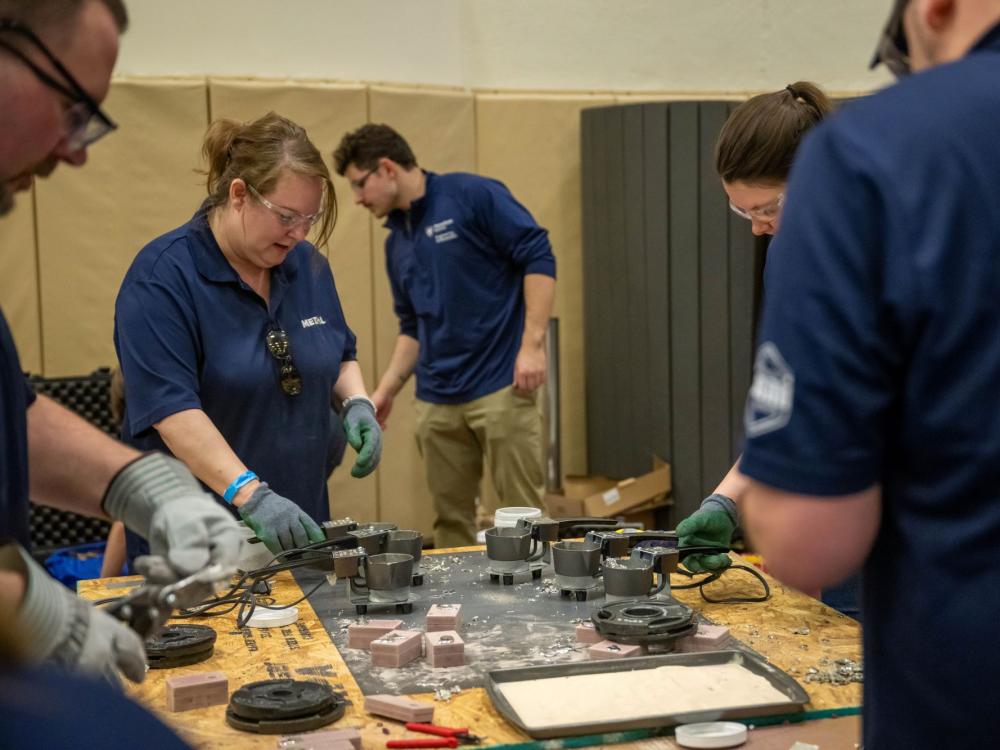 People work around a table covered in tools and metal