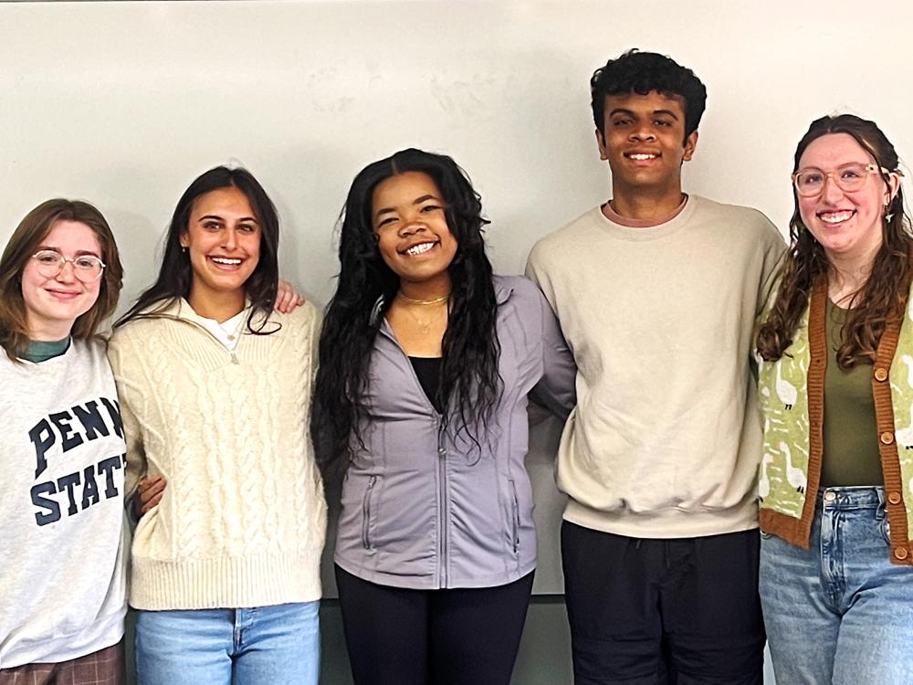 Five people face the camera and smile