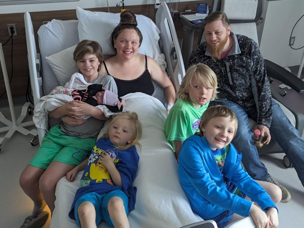 A family gathers around a hospital bed and smiles.