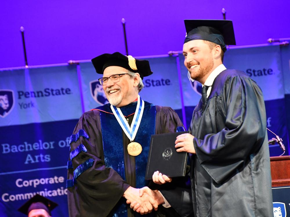 Two men in regalia shaking hands at a graduation ceremony. 