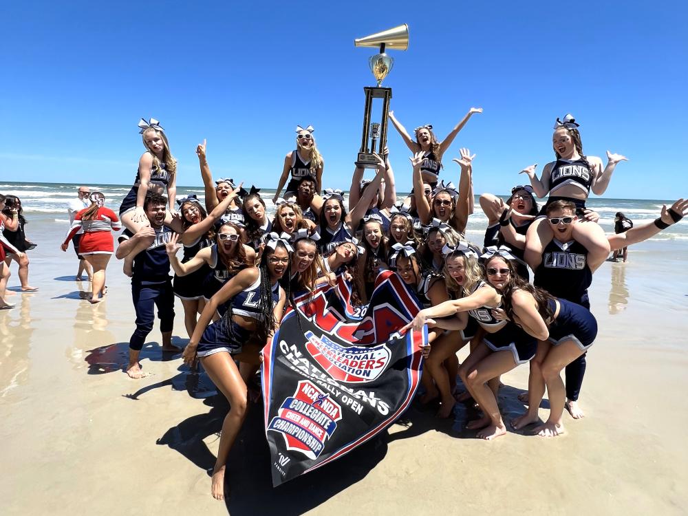 The Penn State Behrend cheer team holds the trophy on the beach in Florida.