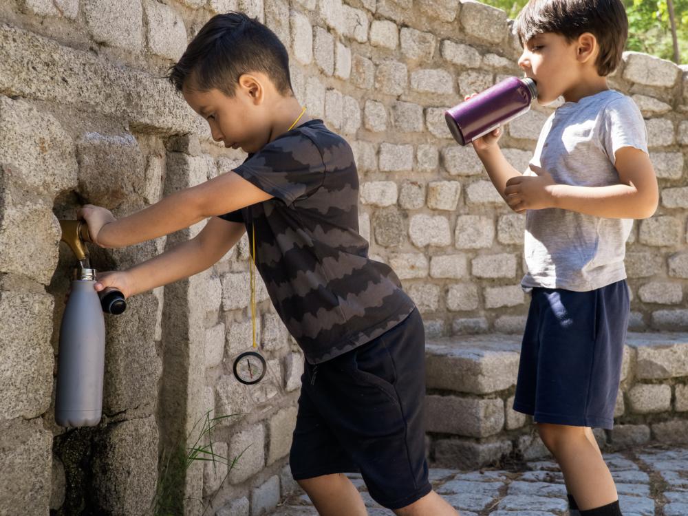 Two children filling water at an outdoor spigot