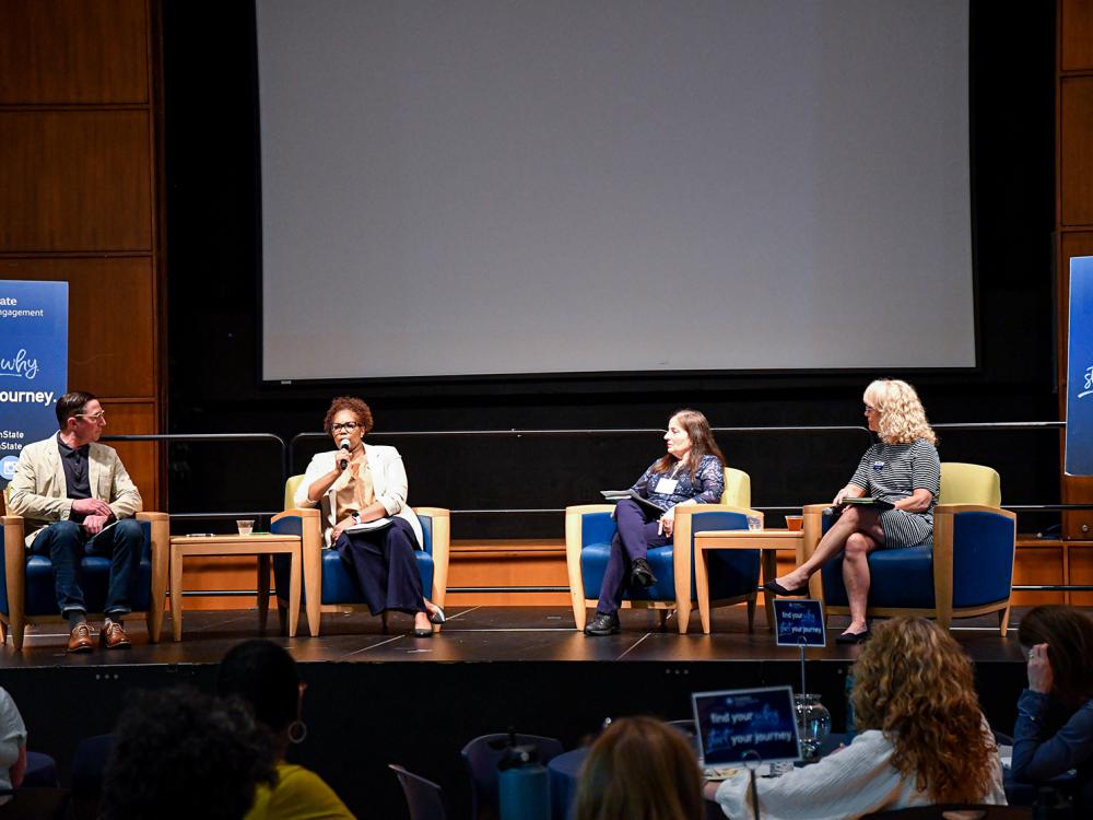 Four people sit on stage, presenting to the audience