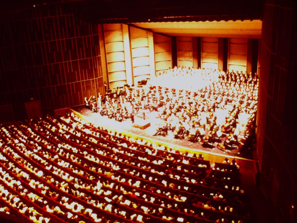 An archival image from a balcony view shows an audience seated in the orchestra section.