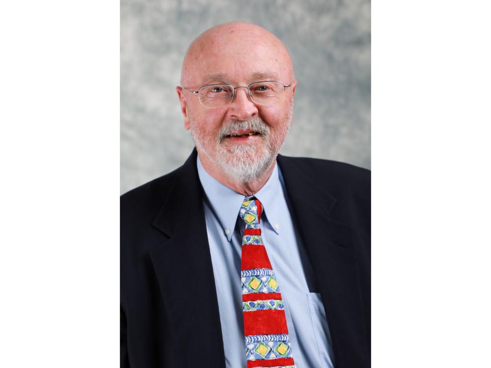 Person with glasses, white beard wearing suit, tie