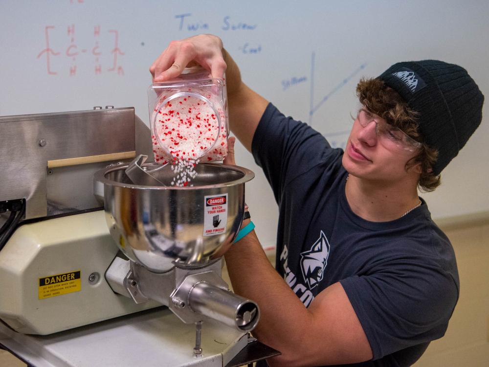 A student pours polymer pieces into a machine