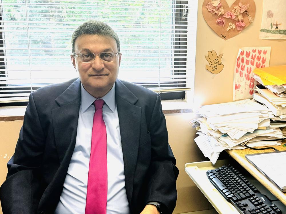 Mookerjee, wearing black suit, white shirt and red tie, sits at a desk in his office.